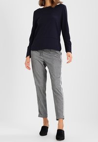 Tmavě modrý top s dlouhými rukávy a kulatým výstřihem, doplněný šedými zúženými kalhotami s károvaným vzorem a bílými bočními pruhy. Černé nazouvací boty.