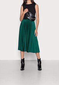 Musta hihaton toppi, vihreä laskostettu midi-hame ja mustat nilkkurit. Asusteina musta olkalaukku, jossa on ketjuolkaimet.