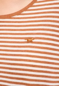 Nahaufnahme eines braun-weiß gestreiften Hemdes mit kleinem gesticktem Pferdelogo auf der Brust.