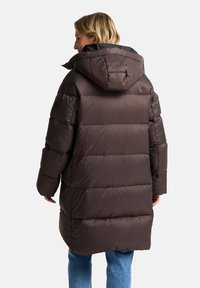 Lange, pufferjas in donkerbruin met gestikte panelen en een capuchon. Beschikt over een gladde, glanzende textuur en een licht oversized pasvorm.