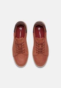 Sneaker in camoscio marrone con punta rotonda, lacci piatti, collare imbottito e suola in gomma bianca. Interno rosso con dettaglio del logo.
