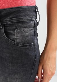 Jeans de mezclilla negros de tiro alto con una textura suave, bolsillo trasero visible y presillas para cinturón, que presentan un efecto de desgaste gradual.