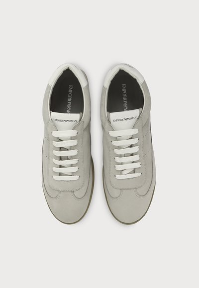 Paire de baskets Emporio Armani gris clair vues de dessus avec des lacets blancs et des languettes brandées sur un fond uni.
