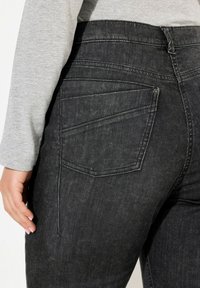 Jeans in denim nero con vita alta, dotati di tasche posteriori angolate e vestibilità slim. Il tessuto presenta una texture sottile e una finitura sbiadita.