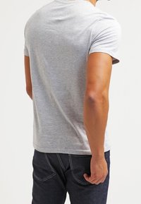 T-shirt in cotone grigio con collo rotondo e maniche corte, caratterizzato da una vestibilità classica e una texture liscia, abbinato a jeans in denim scuri.
