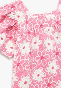 Lyserød blomstret top med et tekstureret stof og hvide samt mørkere lyserøde blomstermønstre. Designet inkluderer puffærmer og en firkantet udskæring.