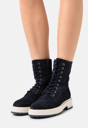 Bottes en daim noir à lacets avec une semelle épaisse blanche contrastante et une fermeture éclair sur le côté ; comprend des œillets en métal et une tige texturée.