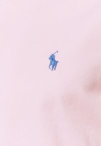 Polo shirt rose avec un logo de joueur de polo bleu brodé. Texture douce avec un design de col classique.