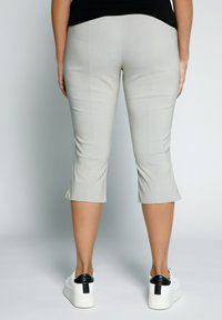 Světle šedé capri kalhoty se slim fit designem a jemnou strukturou. Na sobě má bílé tenisky se černým akcentem na patě.