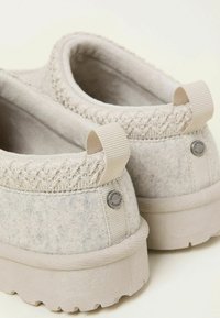 Grey felt slip-on shoes with light fabric accents, textured stitching at the collar, and a patterned rubber sole. Two small pull tabs at the back.