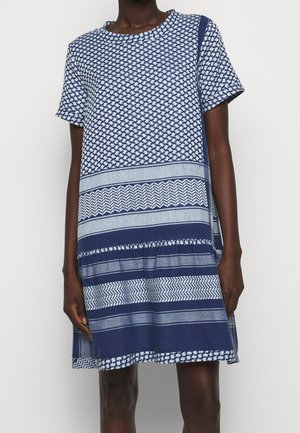 Robe courte à manches courtes longueur genou, bleu et blanc avec des motifs géométriques et rayés, portée par une personne debout.