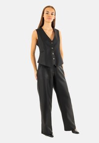 Gilet nero su misura con scollo a V, cinque bottoni e dettagli con tasche abbinato a pantaloni a gamba larga coordinati. Finitura liscia e design strutturato.