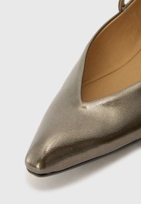 Chaussure pointue en gris métallique au design épuré, avec un détail découpé et une texture lisse. L'intérieur est doublé de beige.