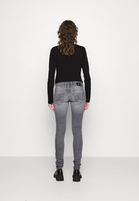 Jeans skinny grises con un acabado desgastado, bolsillos con botones y una pequeña etiqueta de logo negra; combinados con una camiseta ajustada de manga larga negra y zapatos negros.