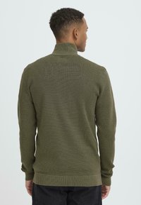 Zaļolīvu adītu džemperi ar augstu apkakli, ribotām piedurknēm un apakšmalu. Teksturēta auduma ar smalku rakstu, pieguļoša dizaina.