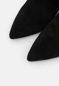 Czarne zamszowe buty na szpilce z ostro zakończonym noskiem, charakteryzujące się gładką teksturą i wyrazistym kształtem, z elegancką cholewką i minimalnymi detalami.