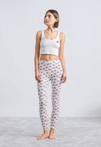 Crop top blanc avec un petit motif de papillon, associé à des leggings gris clair ornés d'un imprimé cerise. Tissu lisse, silhouette ajustée.