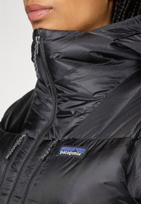 Vrouw in een zwart Patagonia geïsoleerd jack met hoge kraag en twee verticale ritssluitingen op de borst.