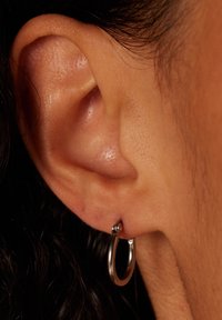 Zilveren hoepel oorbel met een gepolijst afwerking, voorzien van een kleine bolvormige accent bovenaan, weergegeven tegen een close-up van de huid.