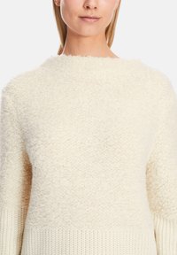Cream-colored sweater featuring a fluffy texture, round neckline, and ribbed cuffs, with a soft, cozy appearance.
