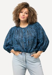 Blusa blu a fantasia con scollatura rotonda, maniche ampie e dettagli con bottoni, abbinata a jeans in denim chiaro a vita alta.