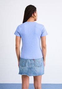 Top scurt cu mânecă, de culoare albastră deschisă, cu dungi, asortat cu o fustă din denim decolorat, cu un tiv despicat și buzunare pe spate.
