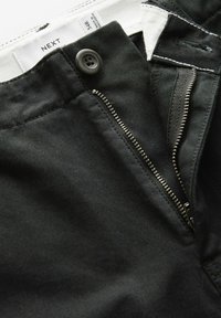 Jeans noirs avec une fermeture éclair à dents métalliques, un bouton de fermeture et une étiquette. Tissu texturé avec des détails de couture visibles.