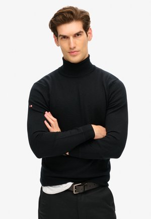 Maglione nero a collo alto realizzato in un tessuto a maglia liscia, con un design aderente e un piccolo logo sulla manica sinistra.