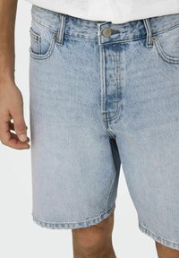 Șorturi din denim de un albastru deschis, cu margini destrămate, design cu cinci buzunare și închidere cu nasture, având un aspect puțin estompat și o textură subtilă.