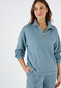 Felpa zip-up di colore azzurro chiaro con colletto alto, dotata di maniche lunghe, tasca frontale e una texture morbida e liscia.