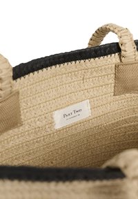 Intérieur d'un sac cabas en paille tissée beige avec deux anses tressées et une étiquette blanche portant l'inscription "Part Two Est Copenhagen 1995."