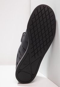 Black athletic shoe sole featuring a textured rubber surface with a diamond pattern and an angular design. Durable material and flat profile.