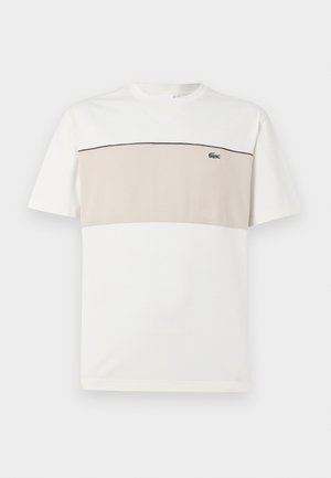 T-Shirt mit kurzen Ärmeln in Weiß und Beige. Weiches Baumwollmaterial mit einem runden Ausschnitt und einem genähten schwarzen Akzent über der Brust. Lacoste-Logo vorhanden.