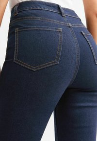 Jeans de mezclilla azul oscuro con una cintura alta, dos bolsillos traseros con costuras naranjas en contraste y una textura suave.