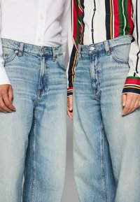 Light blue denim jeans with a relaxed fit, featuring subtle fading, traditional five-pocket design, and top button closure.