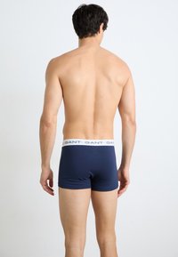 Marineblaue Boxer-Briefs mit einem weißen elastischen Bund, der wiederholt den Markennamen zeigt. Weiches Material, figurbetontes Design mit minimalen Nähten.