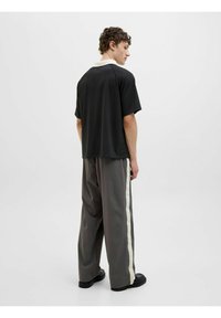 Sort t-shirt med korte ærmer og en cremet krave, parret med løse grå bukser med en hvid stribe i siden. Enkel design, glat stof.
