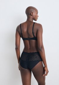 Fekete csipke bralette állítható pántokkal és kampós záródással, magas derekú fekete bugyival párosítva, amelynek csipke díszítése van a derékrészen.