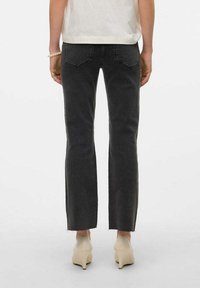 Jeans de mezclilla negra con corte recto, dobladillo sin acabar y dos bolsillos traseros. Llevados con una camiseta blanca y tacones beige.