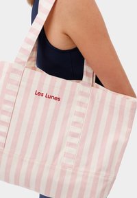 Gestreepte canvas tas in lichtroze en roomwit, met de tekst "Les Lunes" in het rood, twee stevige handvatten en een gestructureerde vorm.