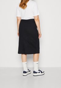 Gonna midi a righe nere con vita aderente, abbinata a una t-shirt bianca e sneakers blu navy. Design semplice, texture liscia e lunghezza fino alla caviglia.