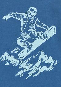 Niebieska koszula z białą grafiką snowboardzisty w powietrzu nad stylizowanymi szczytami gór. Projekt podkreśla dynamikę i ruch.