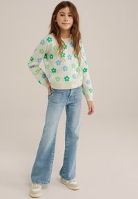 Ljusgrön blommönstrad tröja med blå och gröna blommor, tillsammans med ljusblå utsvängda jeans och beige sneakers med accenter.