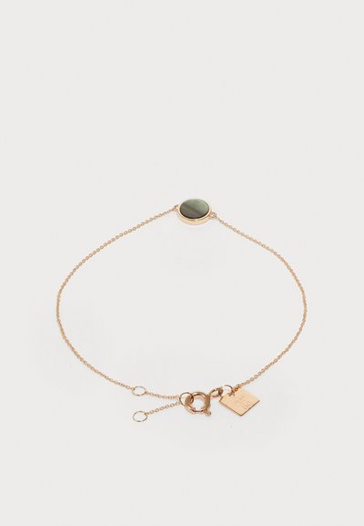 Arany színű karkötő, kerek zöld kő középponttal, texturált lánc kialakítással és állítható kapoccsal, kis címkével.