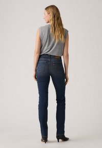 Σκούρο μπλε τζιν με στενή εφαρμογή, που διαθέτουν μέση μέσου ύψους, πίσω τσέπες και καφέ δερμάτινη λεπτομέρεια στο πίσω μέρος, συνδυασμένα με γκρι αμάνικο μπλουζάκι.