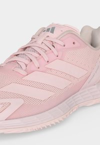 Ροζ αθλητικό παπούτσι Adidas με υφή στην σόλα, τρεις ρίγες στο πλάι και κείμενο «Defiant Speed» κοντά στη φτέρνα, με κλείσιμο με κορδόνια.