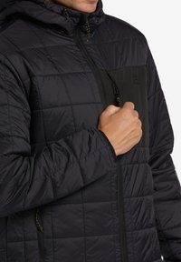 Schwarze steppjacke mit Reißverschluss und Kapuze, ausgestattet mit einer kontrastierenden schwarzen Brusttasche und strukturiertem Stoff.