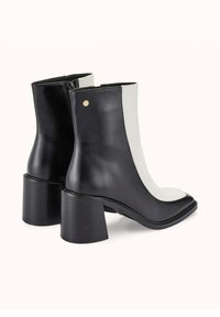 Bottines noires et blanches avec une finition en cuir brillant, bout en amande et talon épais, arborant un accent doré à l'arrière.