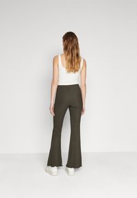 Mørkeoliven vide bukser med struktureret overflade, høj talje og vide ben, paired med hvide platform sneakers og en tætsiddende hvid tank top.