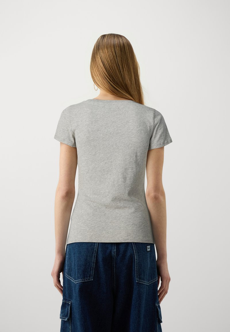 Szara krótki rękaw koszulka z okrągłym dekoltem. Materiał wydaje się miękki i gładki. Noszona z niebieskimi dżinowymi spodniami cargo z kieszeniami.